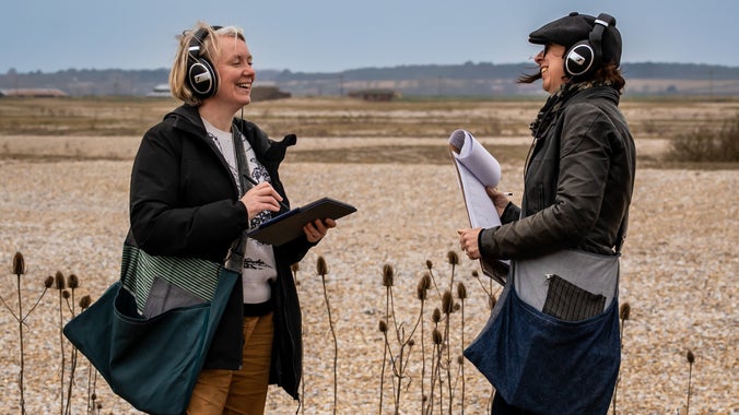 Carolyn Downing and Zoë Svendsen listening to their audio production through headphones on Orford Ness